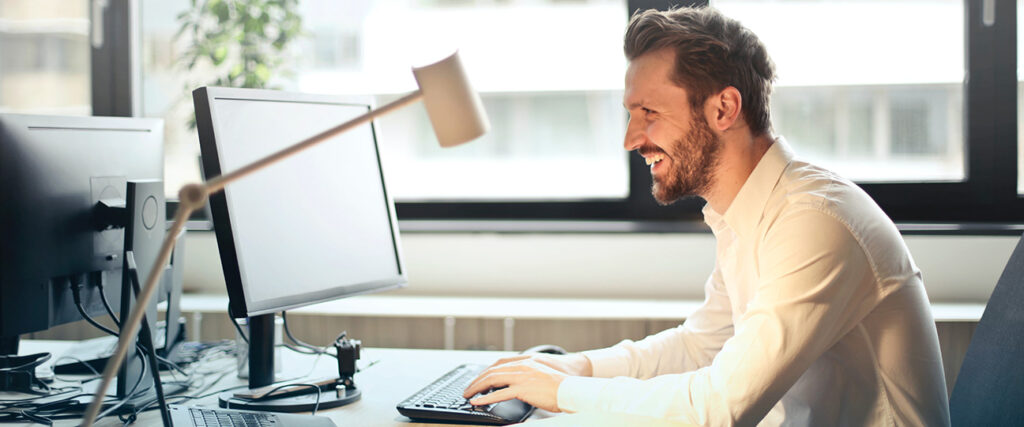 Man in white dress shirt smiling and typing on computer